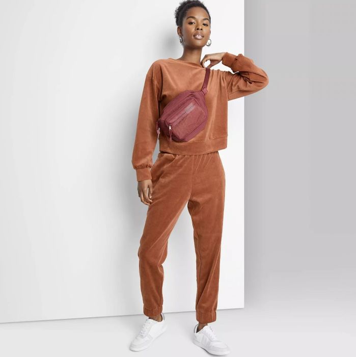 A model wearing orange velour joggers paired with a matching long-sleeve sweatshirt