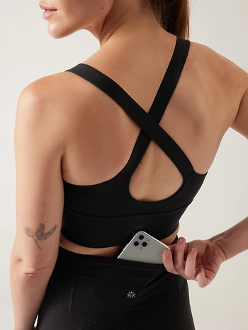 A model demonstrating the hidden pocket in the back of the black leggings by placing their phone inside