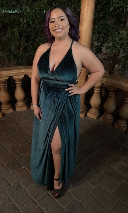 A reviewer is wearing a floor-length green dress with a daring slit.