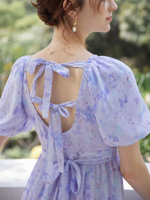 The model is showcasing the back of the dress, adorned with delicate bows.