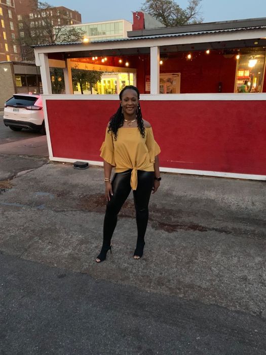 A reviewer is photographed wearing black faux-leather leggings with a yellow top outside a restaurant