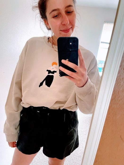 The writer wearing the beige sweatshirt with an embroidered image of Princess Diana in a strapless black dress on the front