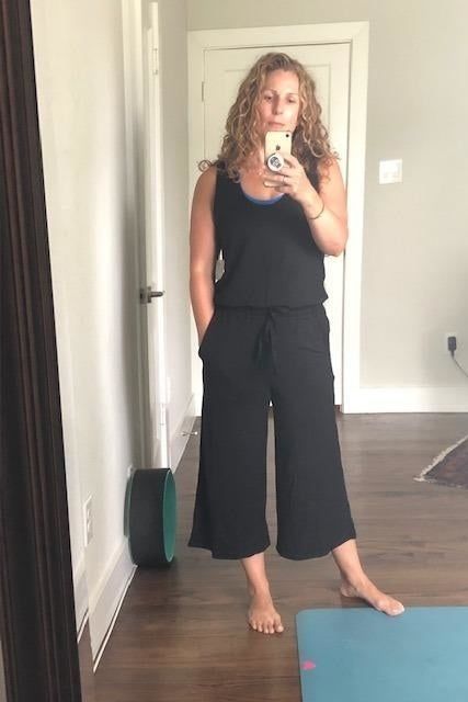 a mirror selfie of a reviewer in a black wide-leg jumpsuit posing next to a workout mat