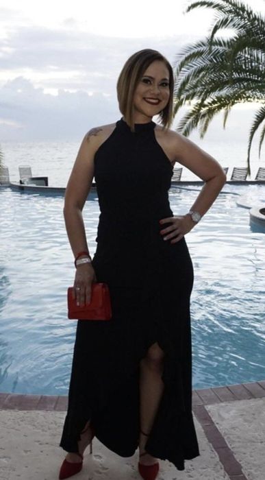 A reviewer flaunts a black sleeveless cocktail dress, boasting a slit that adds a touch of drama to the full-length design.