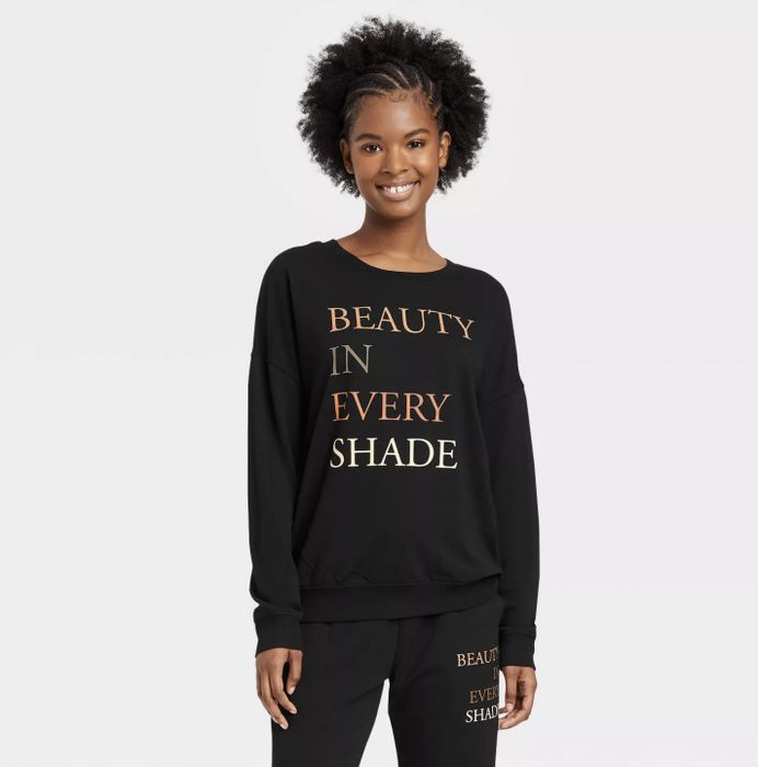 A model wearing a black crewneck sweatshirt with a colorful, bold message
