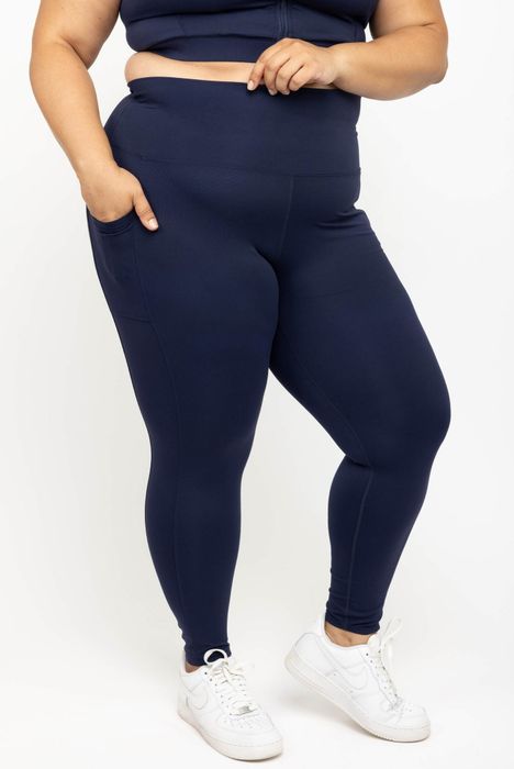 A person styled in navy athletic leggings with pockets and white sneakers, showcasing a sporty look