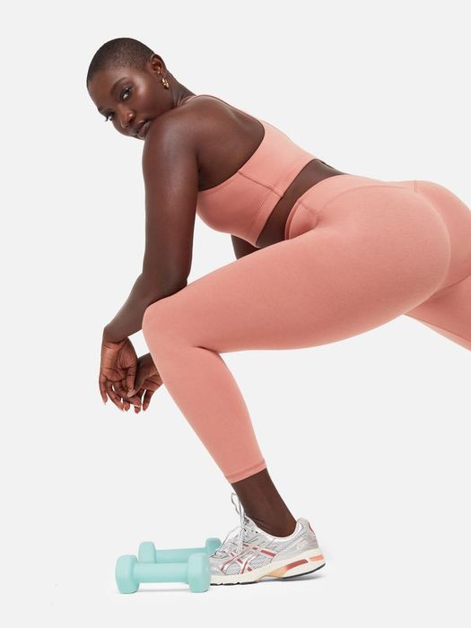 A model performing a lunge in a peachy-pink matching activewear set