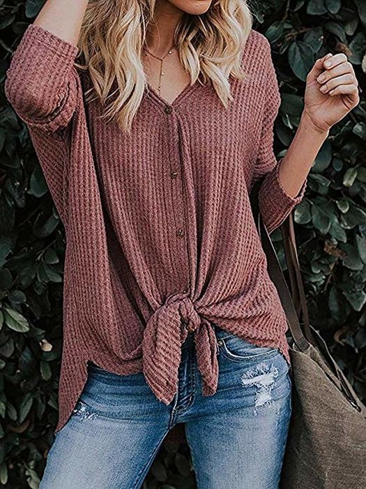 A model styled in a dusty rose waffle-knit button-up shirt with front ties, paired with distressed jeans