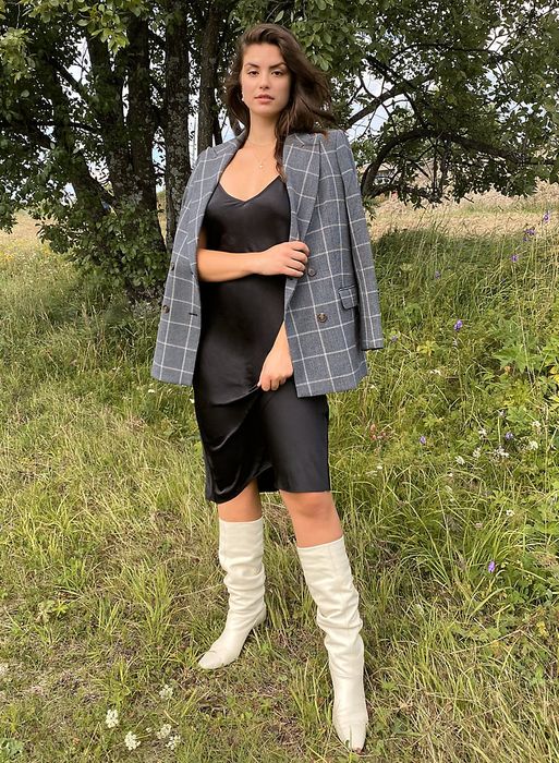 A model wearing a black slip dress paired with a plaid blazer and white boots