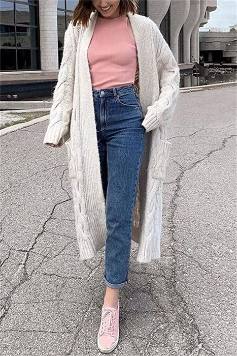 A model dons a long white knit cardigan over a pink tee, matched with blue jeans and pink sneakers.