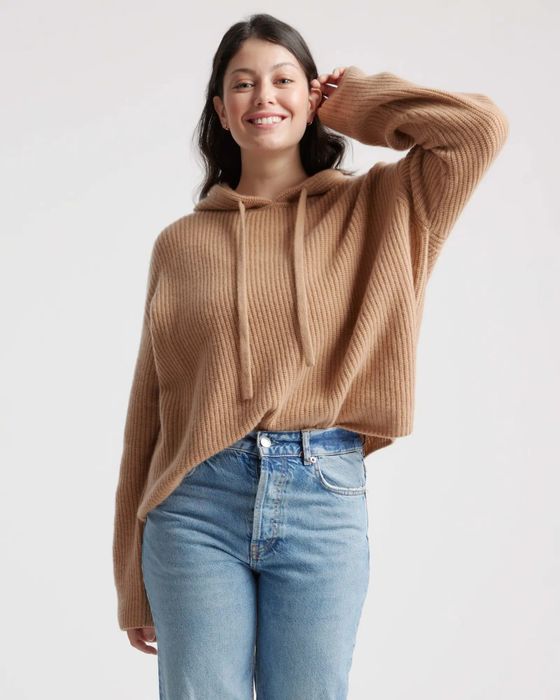 A model is styled in a tan cashmere hoodie paired with blue jeans.