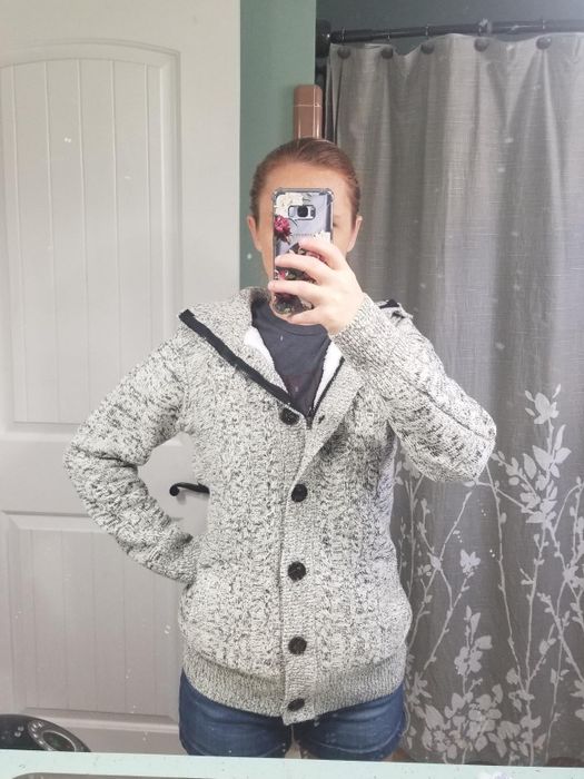 A reviewer shares a photo of themselves wearing a gray button-up knit cardigan.
