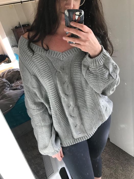 A reviewer shares a photo of themselves in a gray off-the-shoulder cable knit sweater.