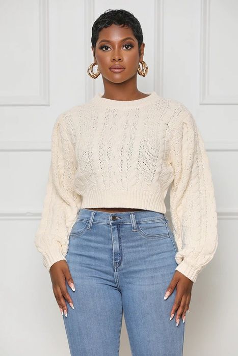 A model wears a cropped white cable knit sweater paired with blue jeans.