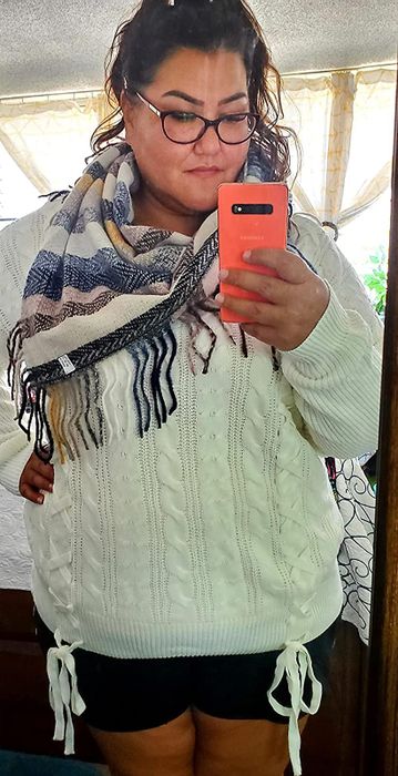 A photo of a reviewer wearing a white cable-knit sweater, featuring ribbon ties at the waist.
