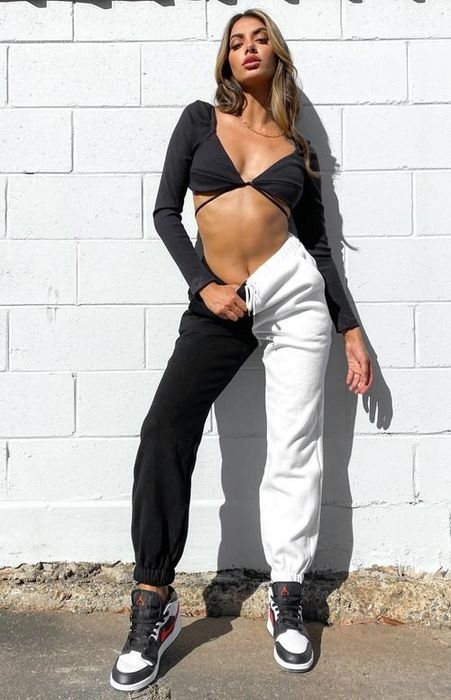 A model wearing a crop top paired with sweatpants featuring one black leg and one white leg