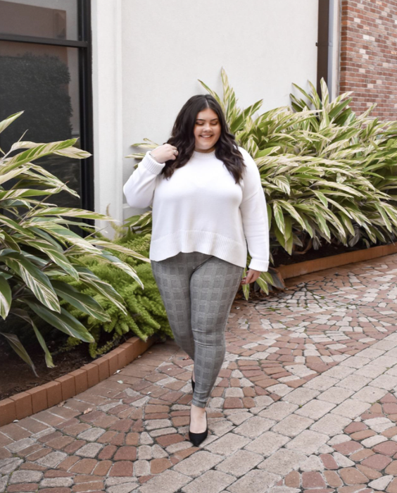 A reviewer wearing gray plaid leggings paired with a white sweater and flats