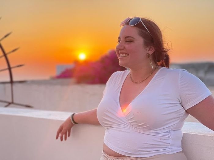 A woman in a casual top smiling with a sunset in the background; ideal for leisurewear shopping content
