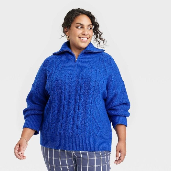 A model is seen wearing a blue cable knit quarter zip sweater.