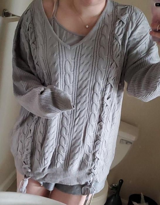 A photo of a reviewer styled in a gray cable-knit sweater with ribbon ties at the waist.