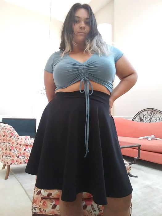The reviewer is seen wearing a light blue drawstring crop top paired with a black flared midi skirt.