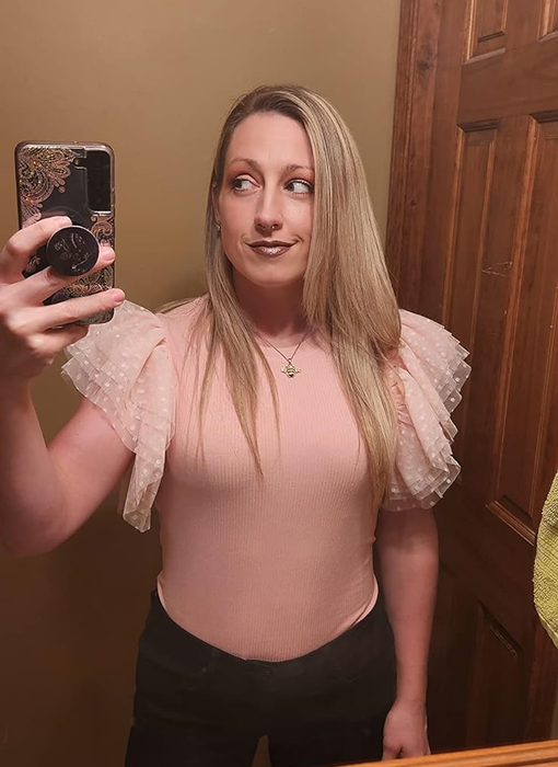 A person snapping a mirror selfie in a pink top with sheer puffy sleeves and black pants, highlighting a stylish outfit idea