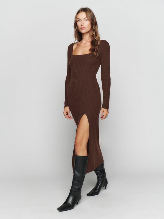 A model dons a brown cable-knit sweater dress featuring a leg slit, paired with black knee-high boots.