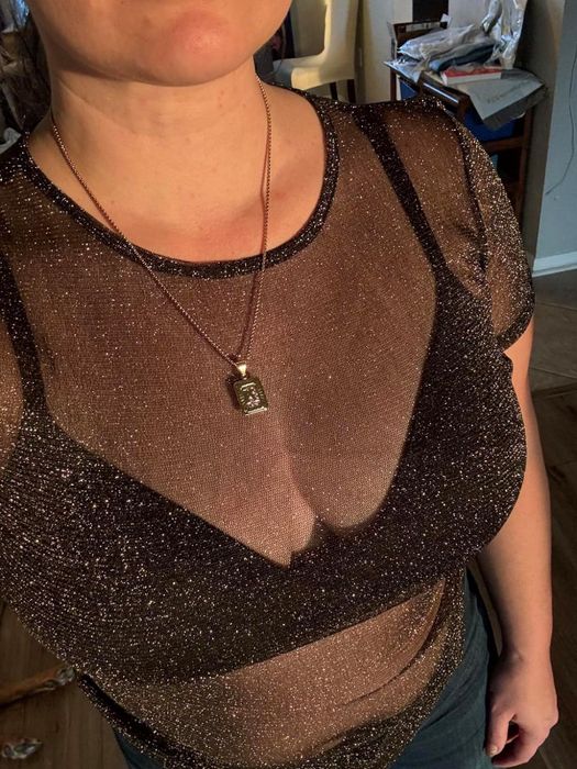 A person wearing a shimmering, semi-transparent top paired with a pendant necklace