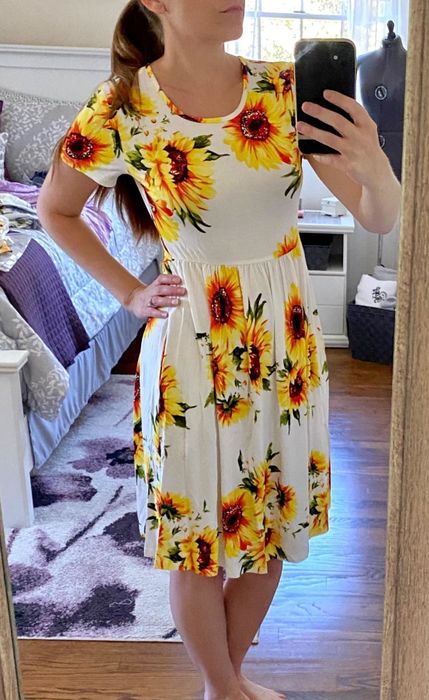 a reviewer modeling the short sleeve skater dress with a cheerful sunflower print