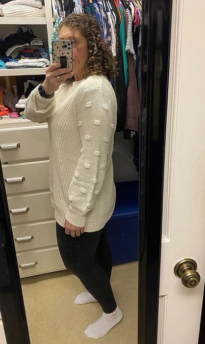 a reviewer modeling the sweater in a clean white shade