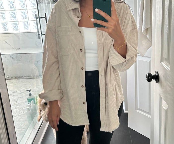 A person wearing a relaxed button-up shirt layered over a top with black pants, capturing a mirror selfie. Ideal for a laid-back shopping day.