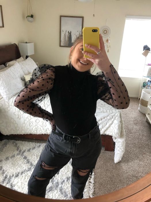 A person taking a mirror selfie in a sheer-sleeved top and ripped jeans, perfect for a stylish fashion post