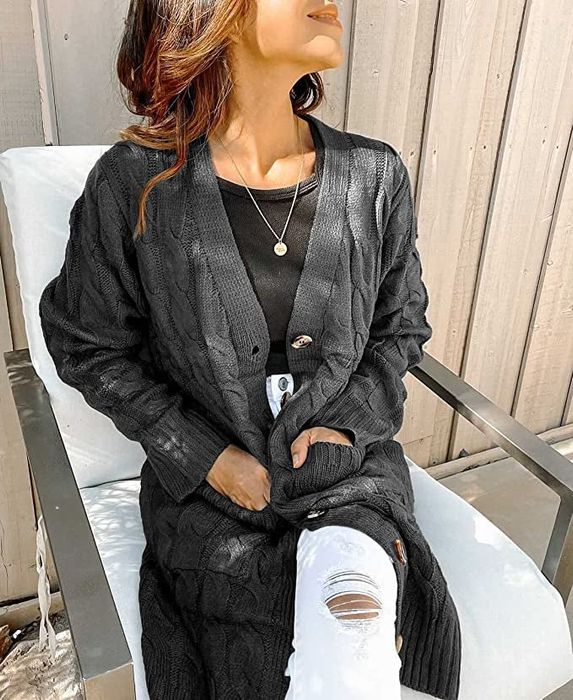 A model sits while wearing a black knit cardigan layered over a black tee and blue jeans.