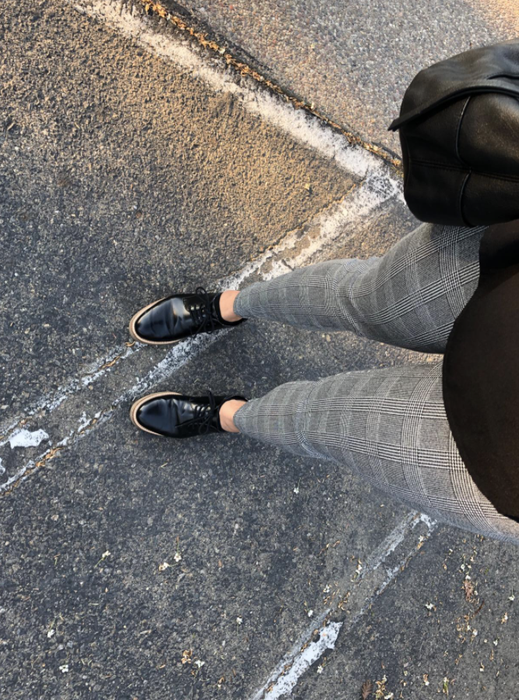 A reviewer taking a photo from above, angled down toward their legs to showcase the gray plaid print