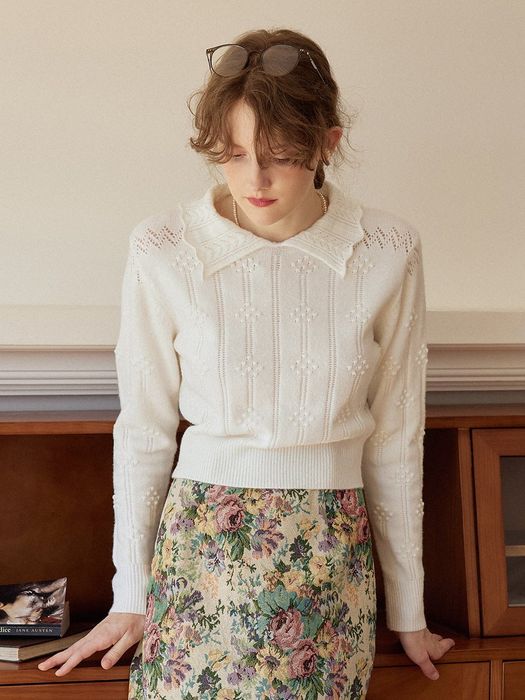 A model is styled in a white knit polo sweater, paired with a floral skirt.