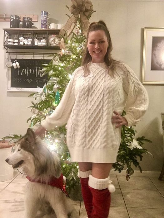 Another reviewer posts a photo of themselves in a white cable knit sweater dress and red boots, standing next to their dog in front of a Christmas tree.