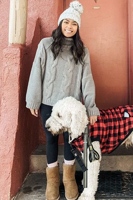Another reviewer shows a photo wearing a gray turtleneck sweater, a white pompom hat, black leggings, and brown boots while standing beside their dog.