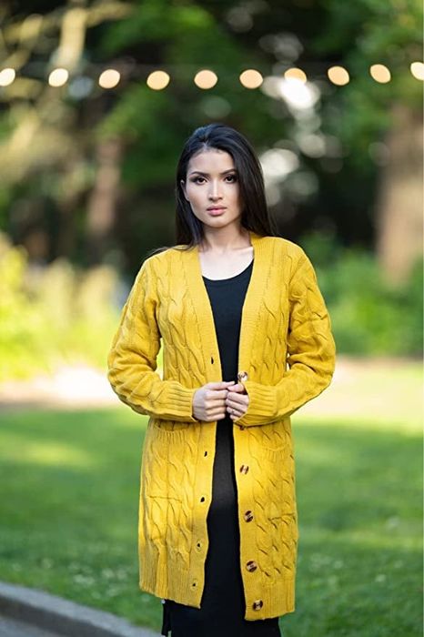 A model pairs a yellow knit cardigan with a black dress for a stylish look.