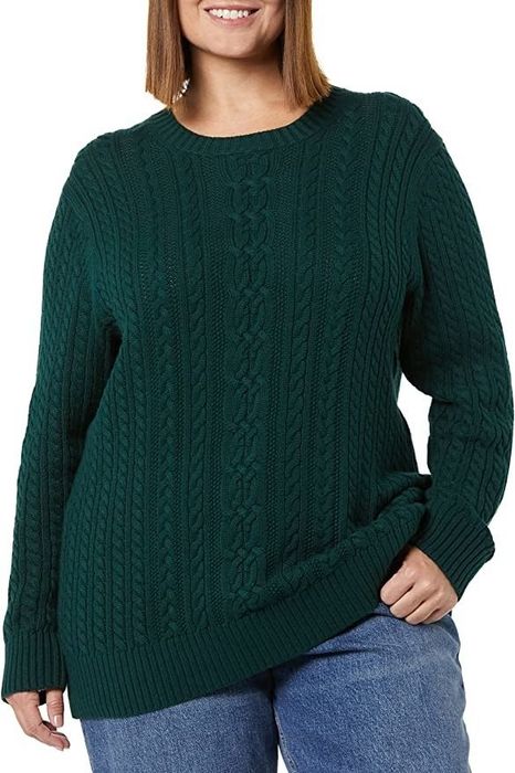 A model is styled in a dark green fisherman cable knit sweater paired with blue jeans.