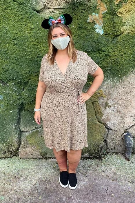 a reviewer sporting Mickey Mouse ears, a face mask, and the cheetah-print surplice dress