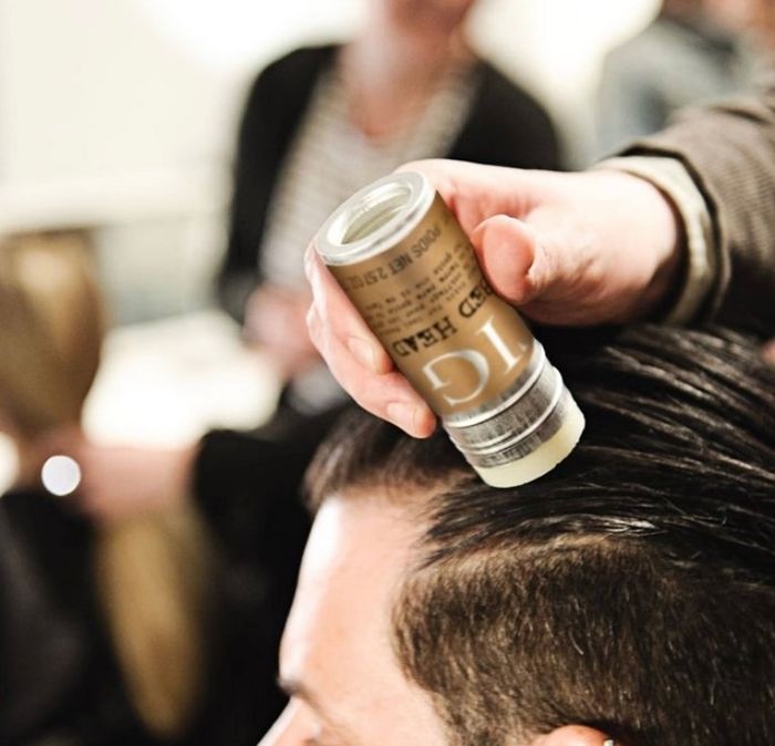 A hand applying the hair wax stick to a person’s hair