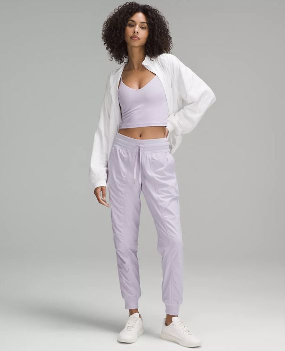 A model stands confidently in a casual athletic outfit consisting of a tank top, jacket, jogger pants, and sneakers. Their curly hair adds to the relaxed, confident vibe of the pose.