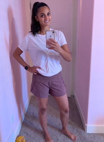A reviewer is seen wearing purple mid-length workout shorts with an elastic waist.