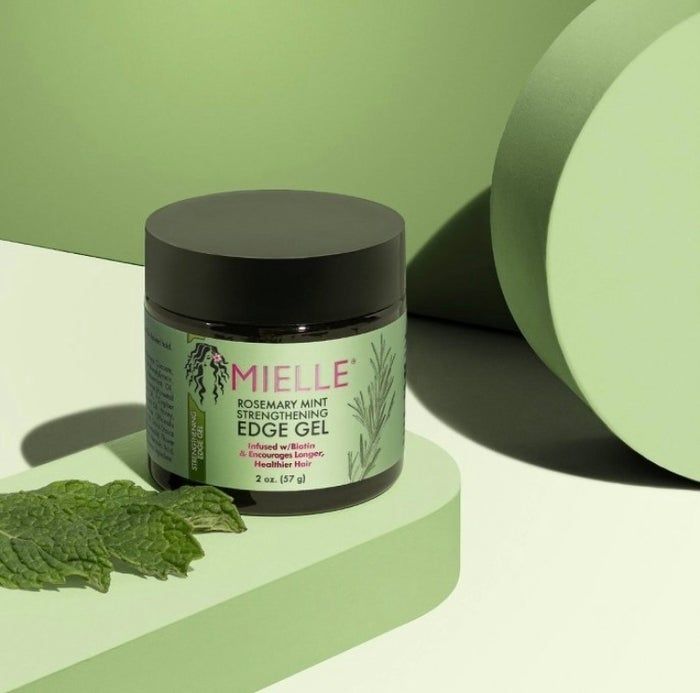 A jar of Mielle Rosemary Mint Strengthening Edge Gel, 2 oz, is displayed alongside fresh mint sprigs