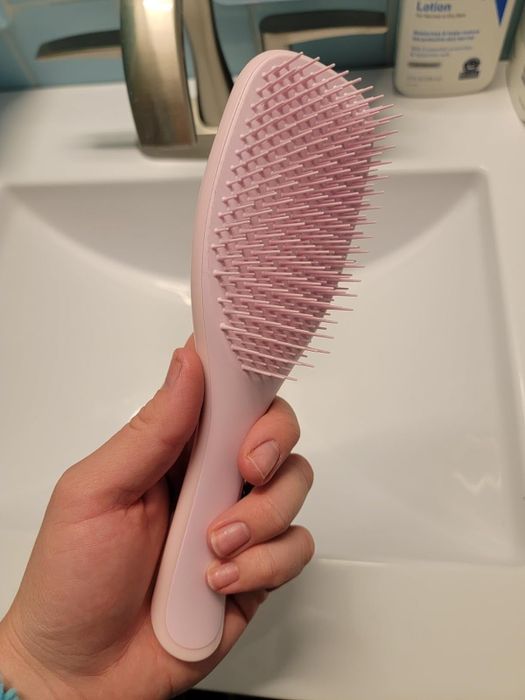 A reviewer showcasing a pink hairbrush in hand