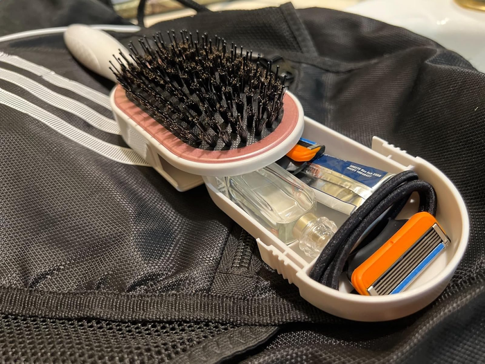 A hairbrush with a hidden storage compartment, showing toiletries and a razor inside, placed on a fabric surface with mesh texture