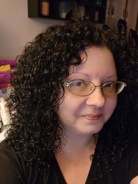 A person with curly hair and glasses smiles at the camera after using the product