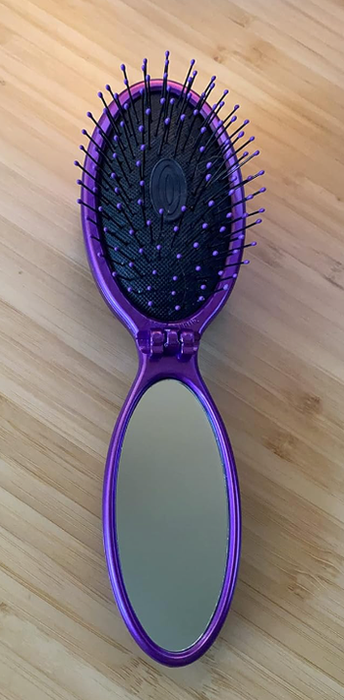 The reviewer’s purple travel brush with a mirror at one end.