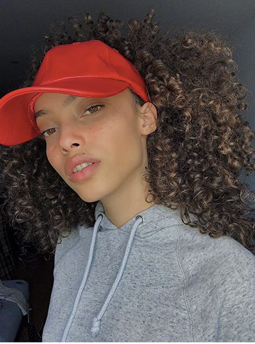 A model is seen wearing a red baseball hat designed with extra space at the back to accommodate curls.