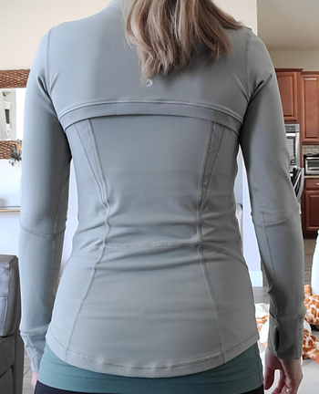 A reviewer displays the back of the gray jacket, highlighting its paneling and seams.